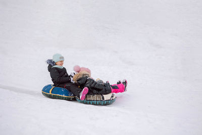 Little girls sledding down hill on walk in winter snowy day.