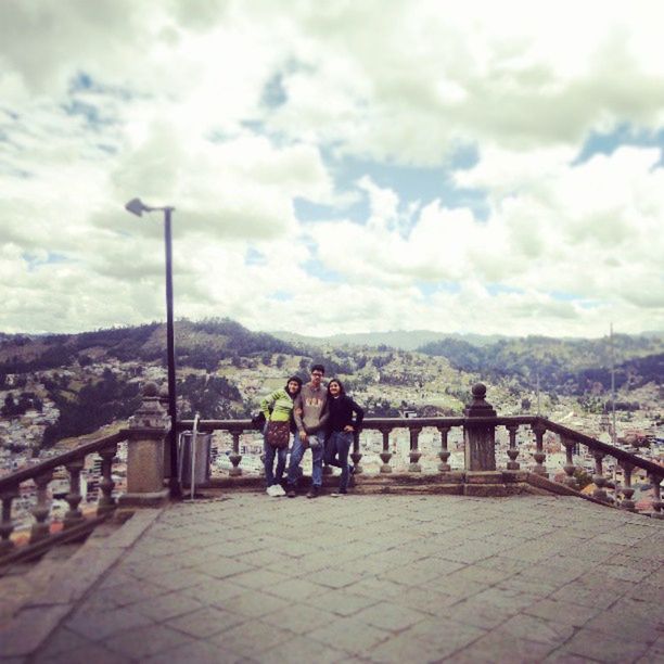 sky, lifestyles, leisure activity, cloud - sky, railing, rear view, full length, men, built structure, person, water, architecture, standing, mountain, togetherness, sitting, casual clothing, cloudy