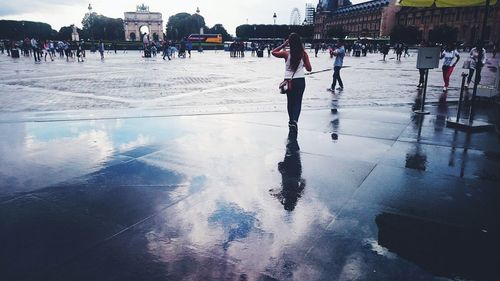 People on wet street in city against sky