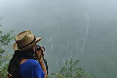 Rear view of woman photographing mountains in foggy weather
