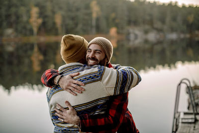 Rear view of man embracing male friend near lake