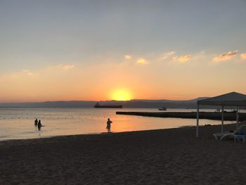 Silhouette people standing on beach against sky during sunset