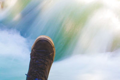 Low section of person wearing shoe against waterfall