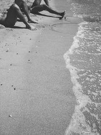 Low section of male friends relaxing on shore at beach