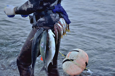 Midsection of fisherman with fish tied on waist in sea