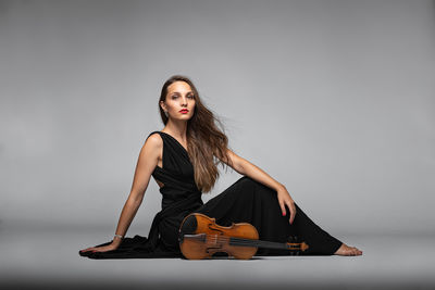Portrait of young woman sitting against gray background