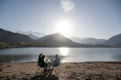 Senior man and his daughter relaxing together sitting outdoors near a lake in nature.