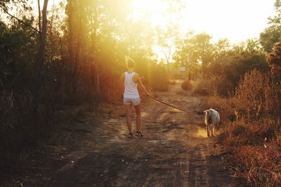 Rear view of woman with dog walking on footpath during sunny day