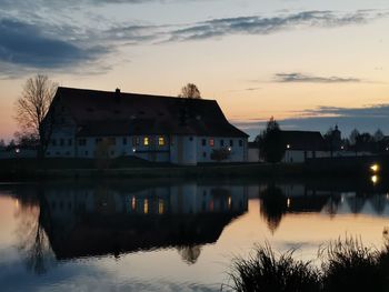 Buildings by lake against sky during sunset