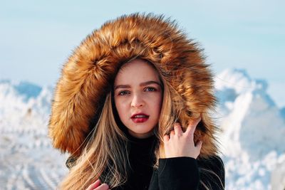 Portrait of young woman wearing fur coat against snowcapped mountains