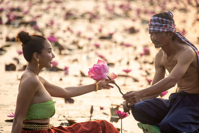 Man giving water lily to woman sitting in boat on lake