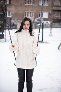 Portrait of young woman swinging in snow covered playground