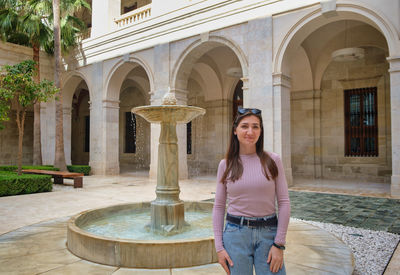 Portrait of young woman standing against historic building