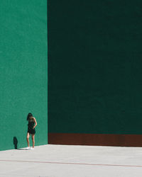 Young woman walking by green wall