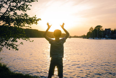 Rear view of silhouette man standing in lake against sky during sunset