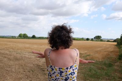 Rear view of woman standing at field against sky