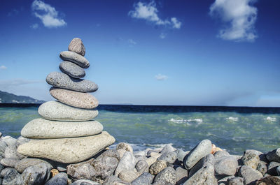 Stack of pebbles by sea against blue sky