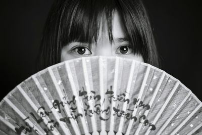 Portrait of young woman holding hand fan against black background