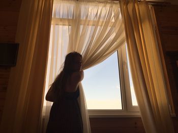 Woman opening curtain at home