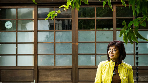Portrait of smiling young woman standing against window