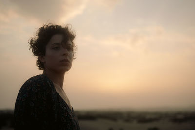 Portrait of young woman standing against sky during sunset