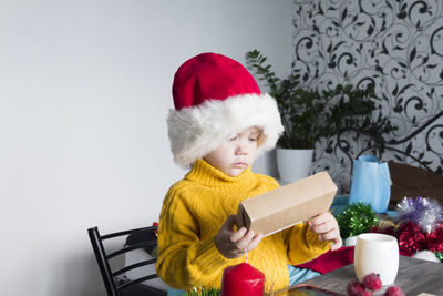 A small child in a yellow sweater and a santa claus hat with gifts on christmas.