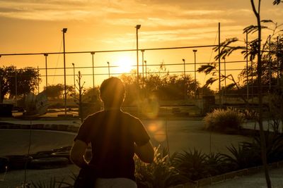 Rear view of silhouette man standing in city against sky during sunset