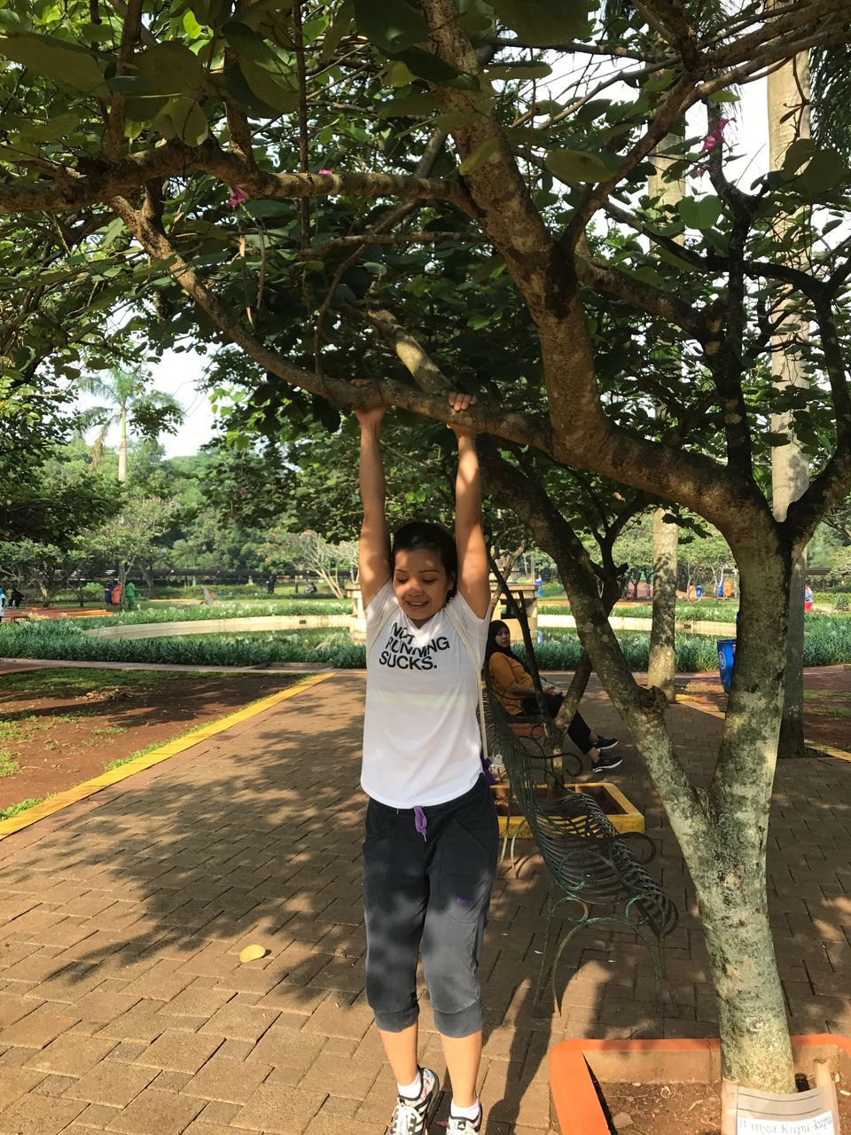 arms raised, tree, real people, one person, full length, front view, casual clothing, leisure activity, lifestyles, day, park - man made space, childhood, happiness, boys, standing, outdoors, looking at camera, young adult, young women