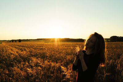 Teenage girl standing on field against sky during sunset