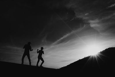 Low angle view of silhouette friends playing on field against sky