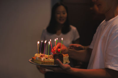 Man holding birthday cake with candles for birthday girl in the house.