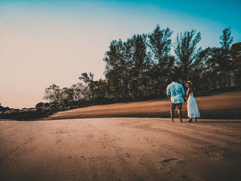 Rear view of couple standing on sand against trees