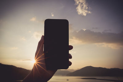 Silhouette person using smart phone against sky during sunset