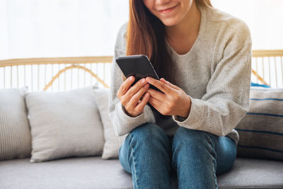 Midsection of woman using mobile phone while sitting on sofa at home