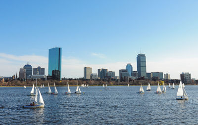 Sailboats in sea by modern buildings against clear sky