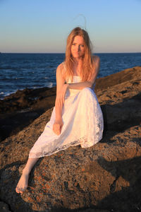 Full length portrait of young woman at beach against sky during sunset