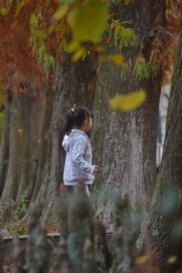 Girl standing by tree trunk in forest