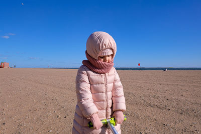 Little girl in a bubble coat dragging her scooter through the sand