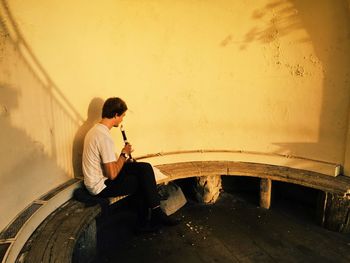 Side view of man sitting against wall