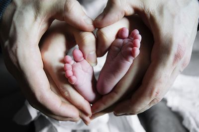 Low section of baby with mother and father making heart shape at home