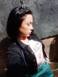 Young woman looking away while standing against wall