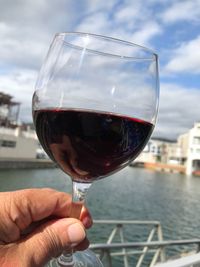 Cropped hand holding wineglass against sea