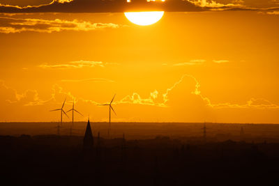 Silhouette wind turbines on land against sky during sunset