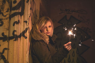 Portrait of woman holding illuminated sparkler in dark