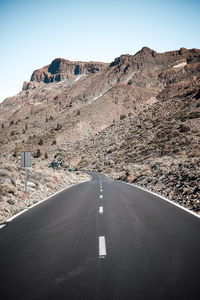 Road leading towards mountains against clear sky