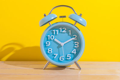 Close-up of clock on table against yellow wall