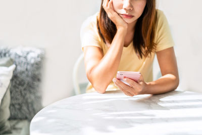 Midsection of woman using mobile phone while sitting by table