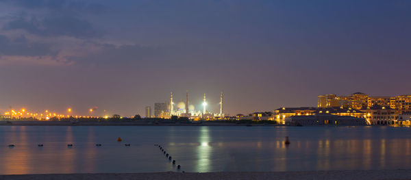 Illuminated city by river against sky at night