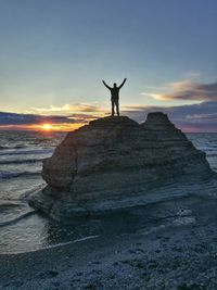 Silhouette man standing on rock at beach against sky during sunset