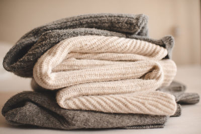 Stack of knitted wool textile sweaters clothes on white blanket in bed at home room close up.